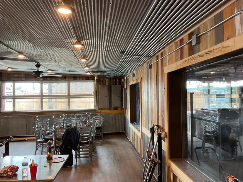 Interior of a rustic restaurant with metal ceiling, wooden walls, and empty dining area.